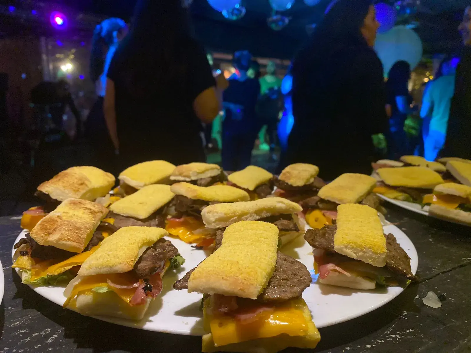 Bandeja de mini chivitos, con la pista de baile iluminada detrás