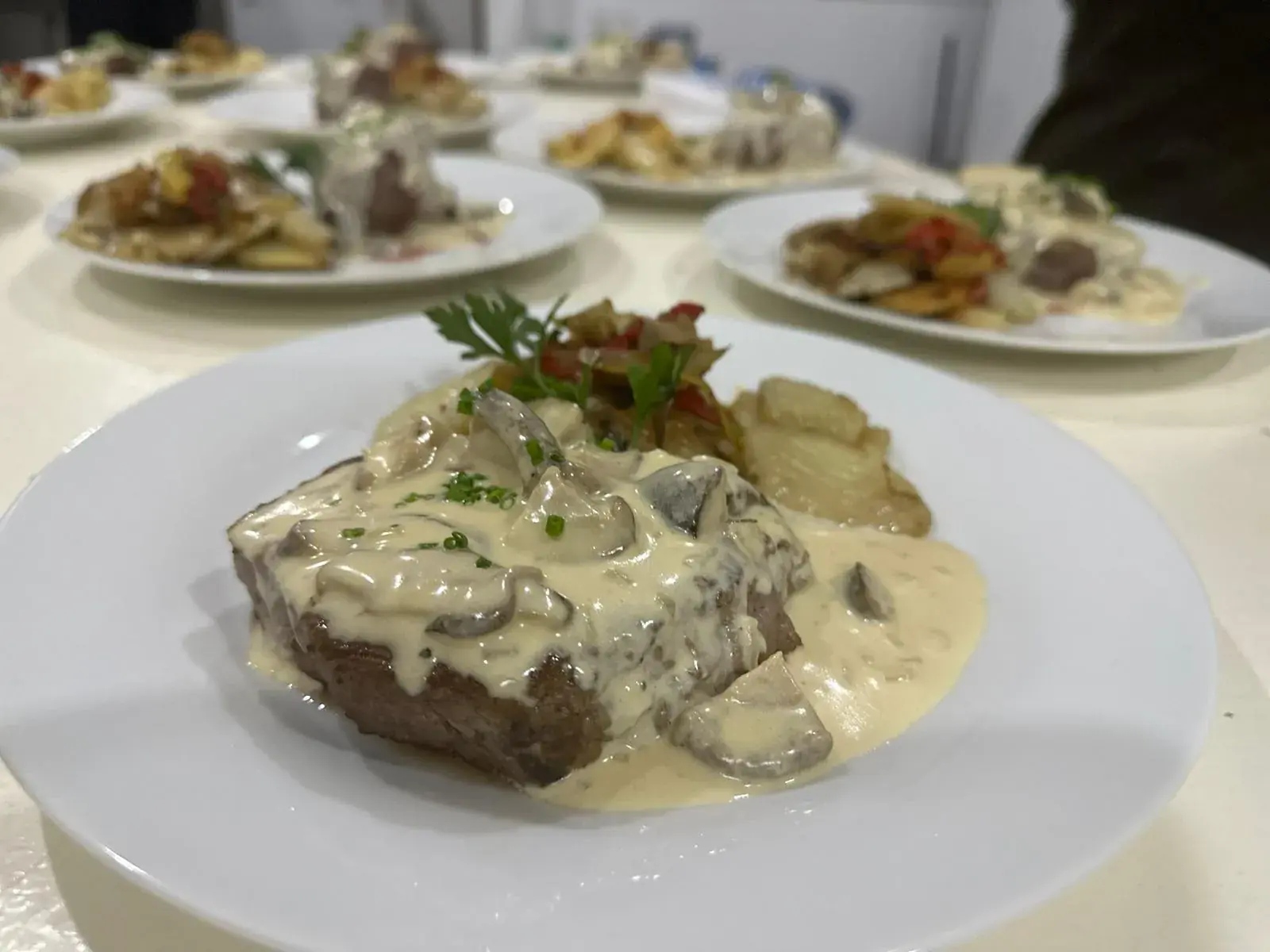Línea de platos emplatados con bife y su guarnición, listos para salir